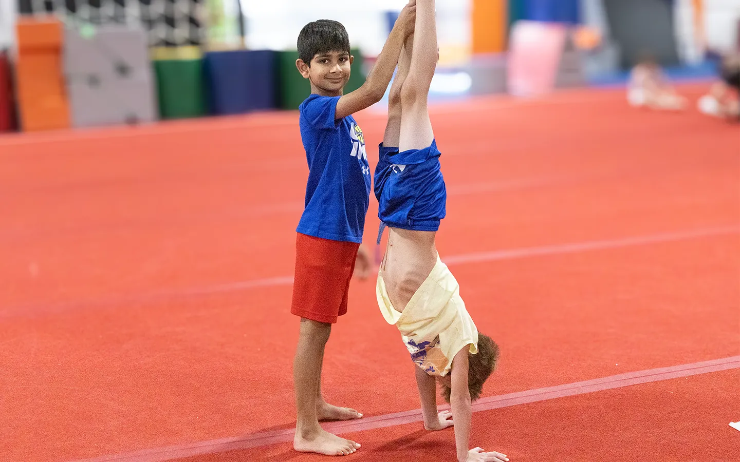 A coach spotting a boy's handstand on the floor at EGA